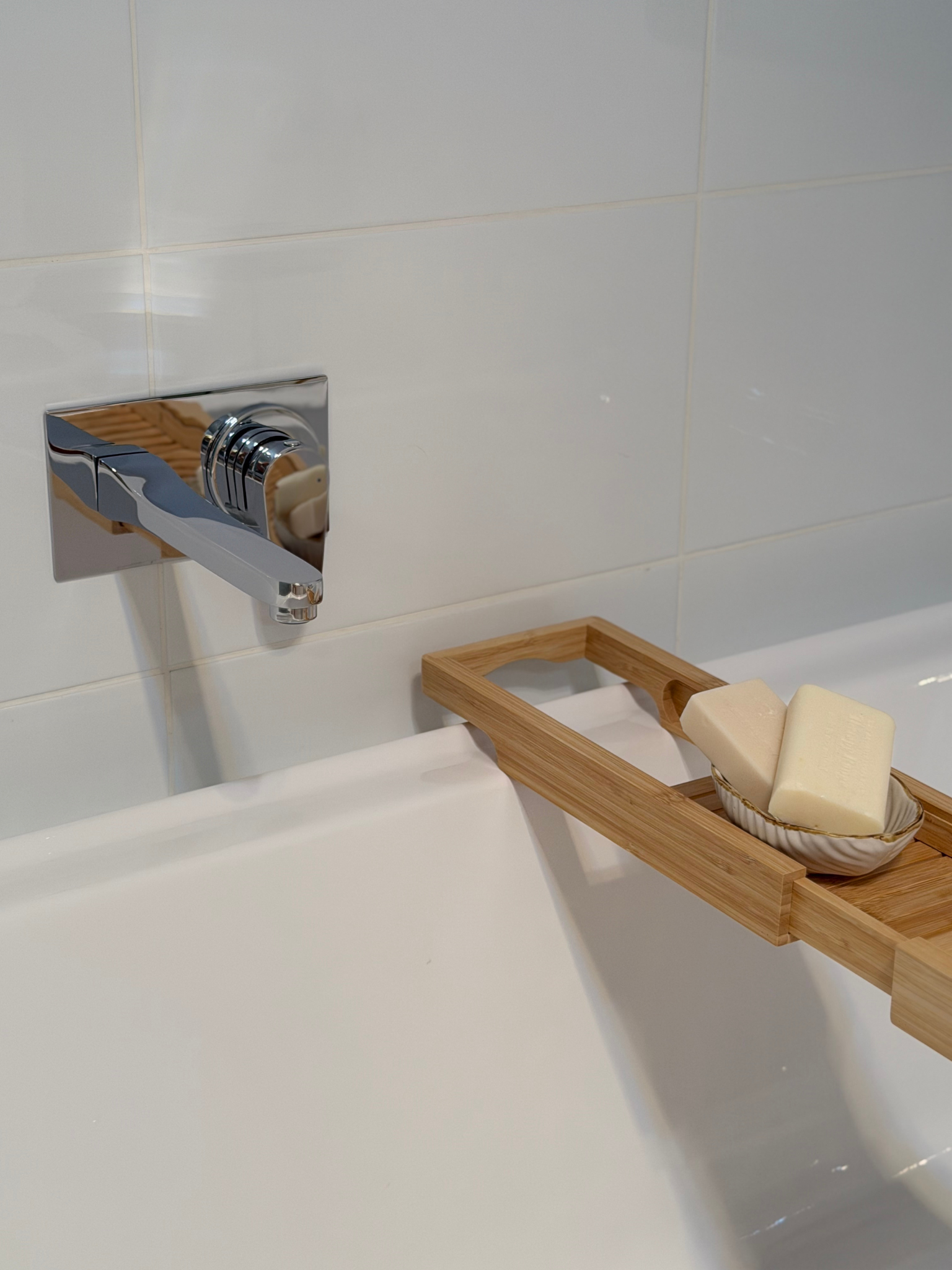 A bathroom sink with a chrome faucet and a wooden tray holding bars of soap.