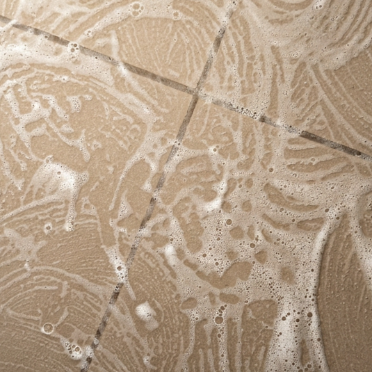 Close-up of beige tiled bathroom floor with soap suds and water