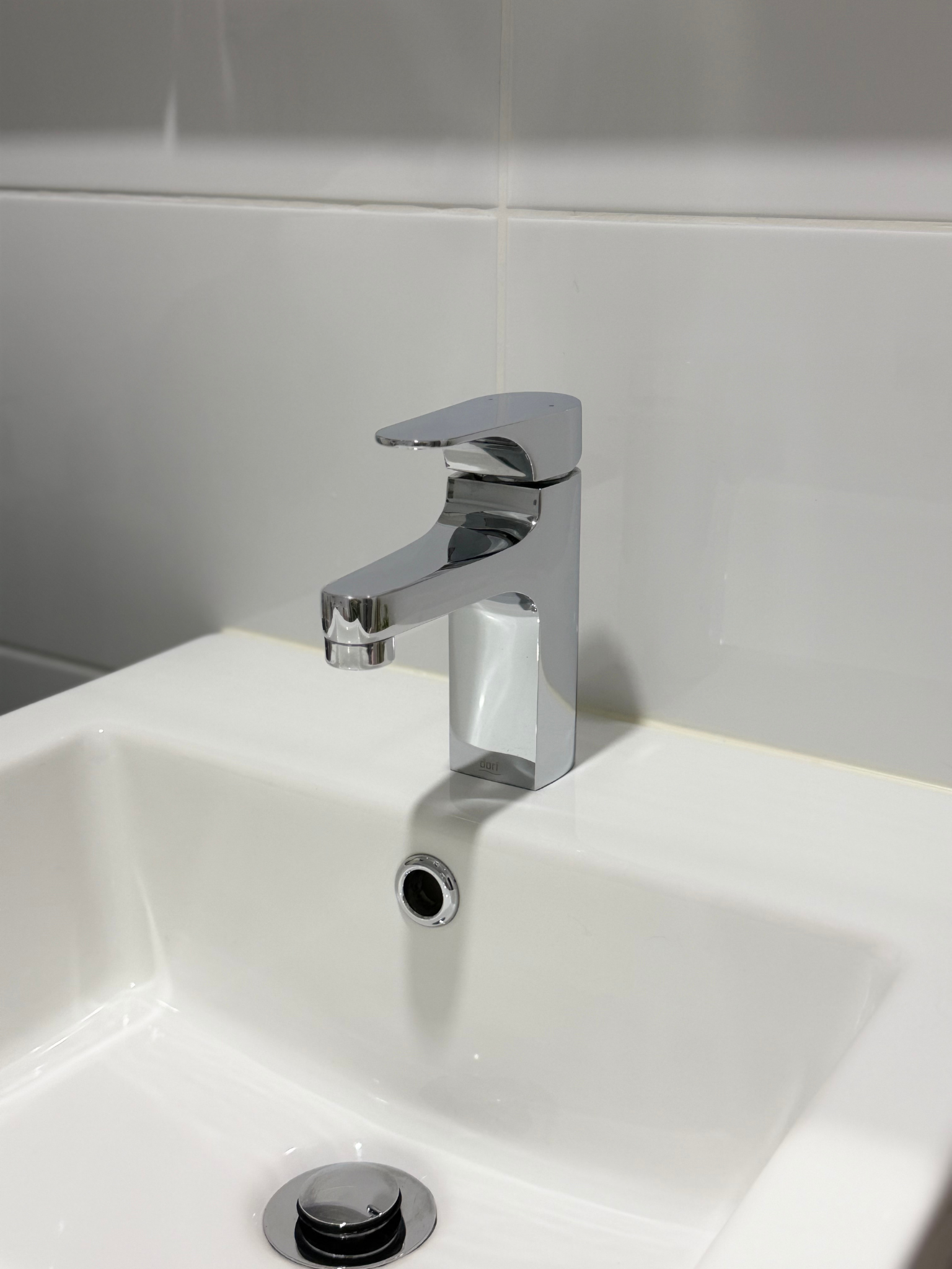 A modern chrome bathroom sink faucet above a white sink with a drain.