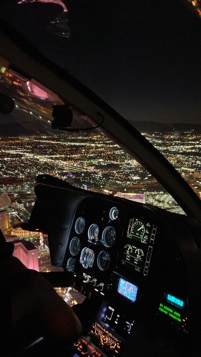 View from an aircraft cockpit at night showing city lights below and the aircraft's controls and instrument panel.