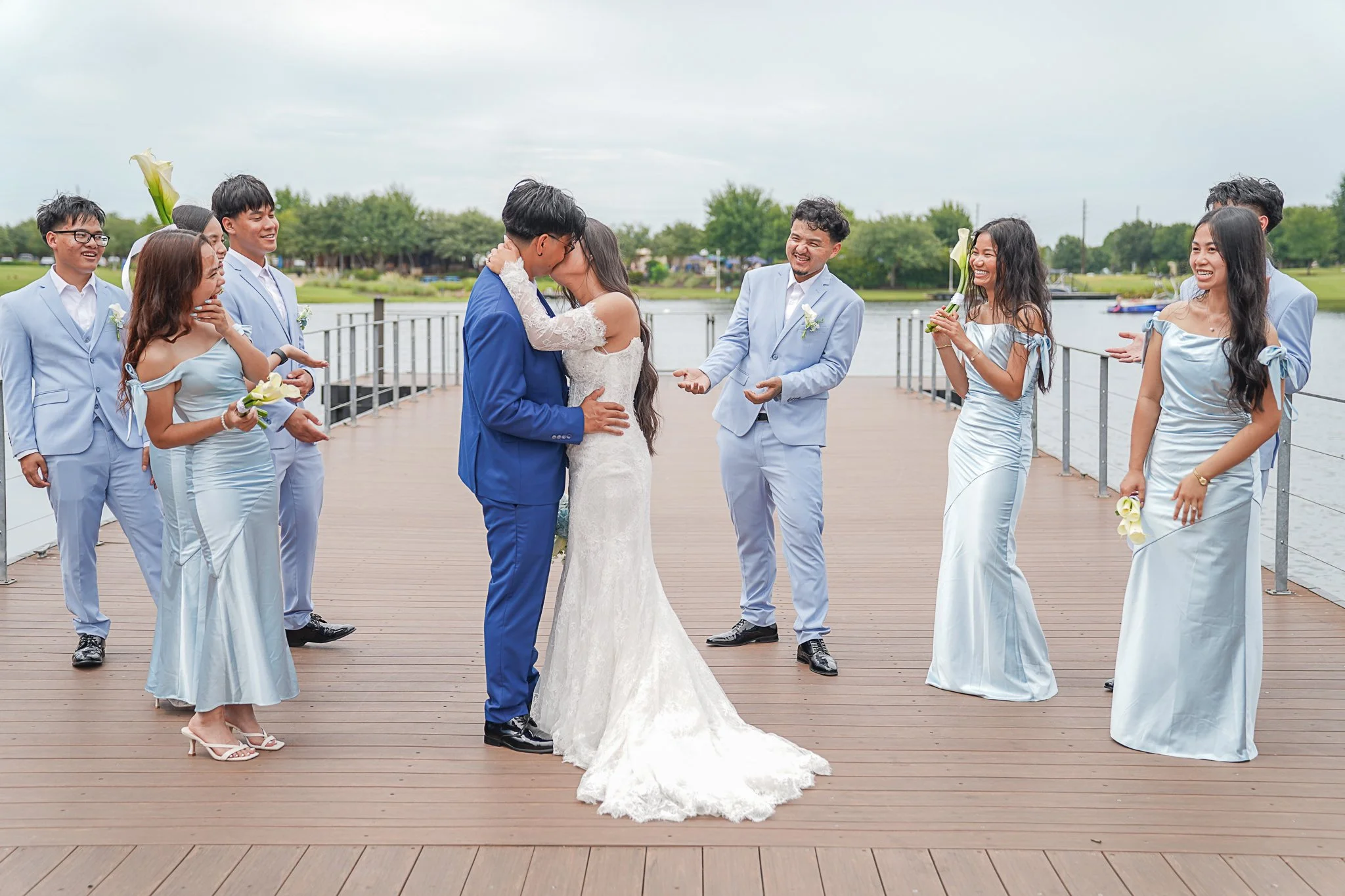 A wedding ceremony by a river with the bride and groom kissing and friends and family smiling and celebrating.