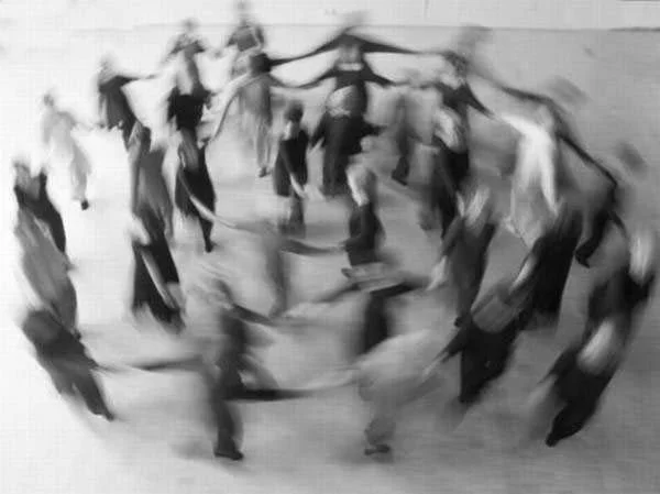 A group of people holding hands in a circle outside, possibly dancing or playing a game.