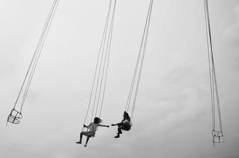 Two children playing on swing sets against a cloudy sky.