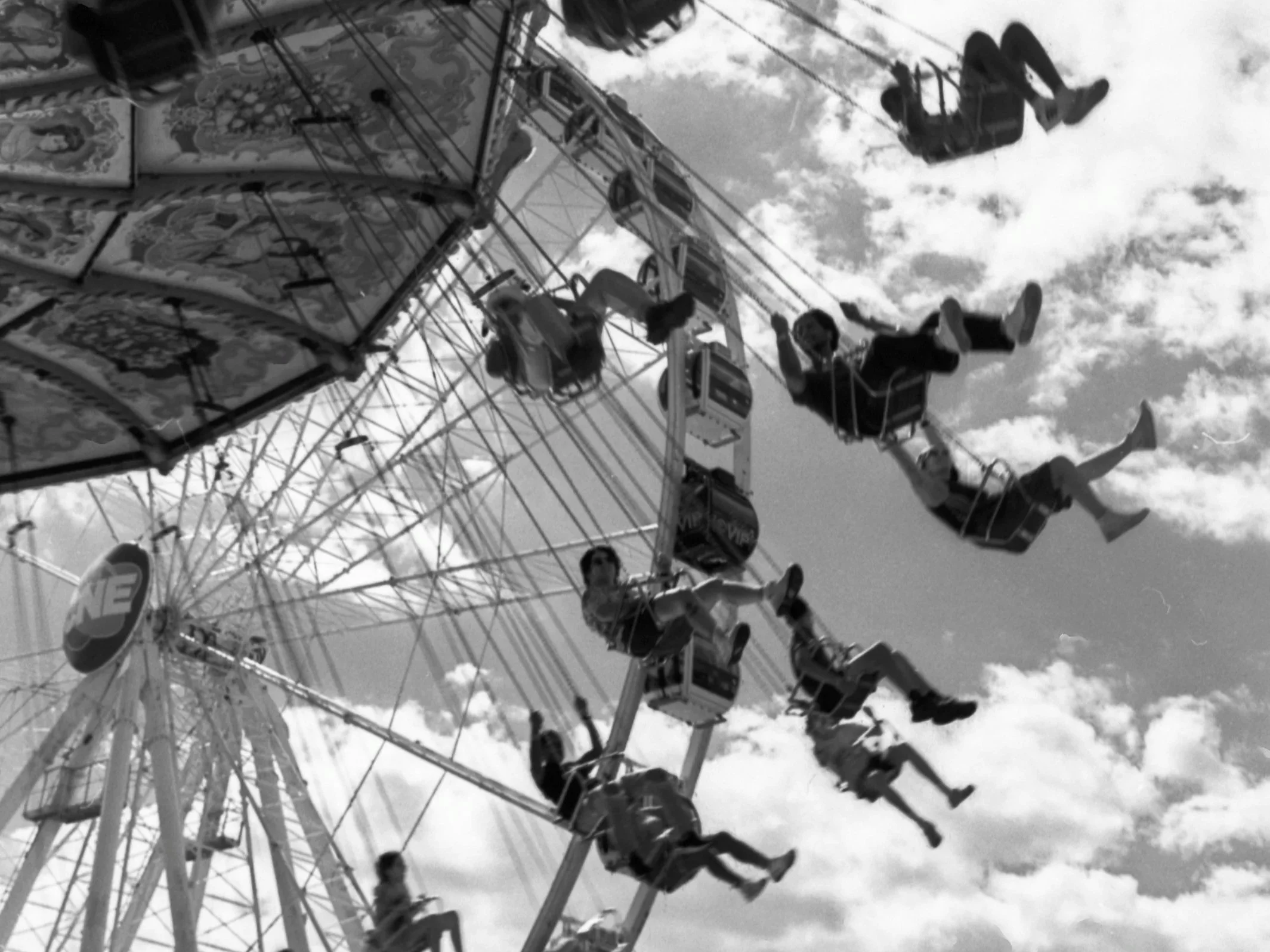 A ferris wheel ride at a fair with people in the gondolas, against a partly cloudy sky.