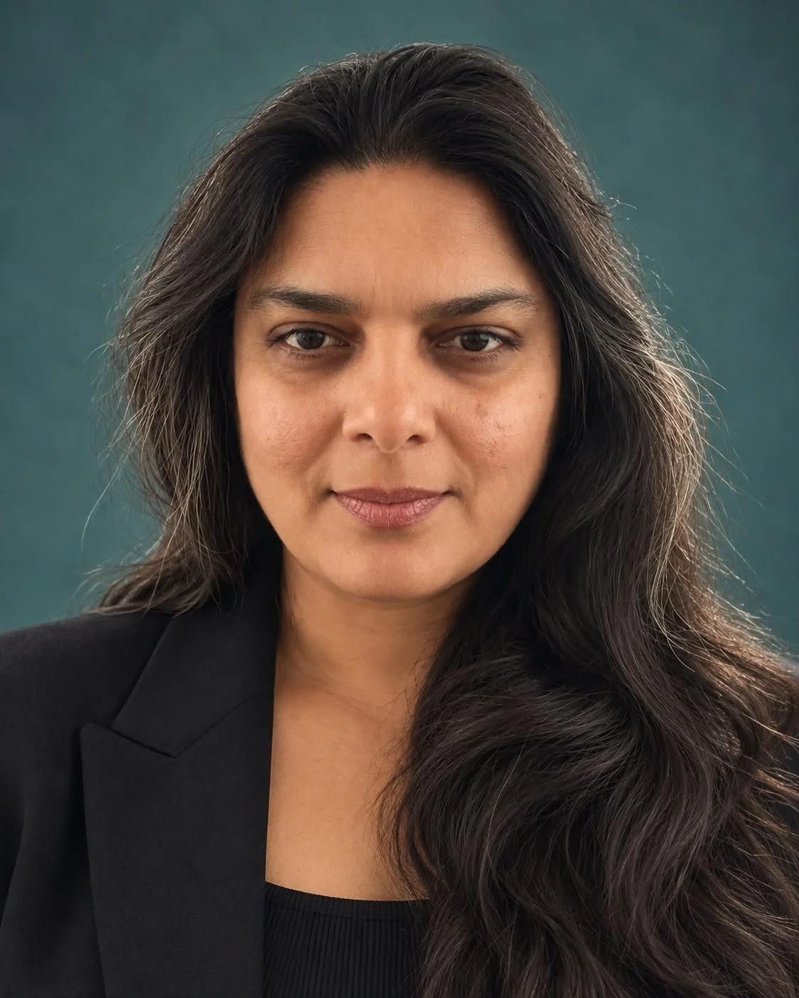 Close-up portrait of a woman with long dark hair, wearing a black blazer, against a greenish background.