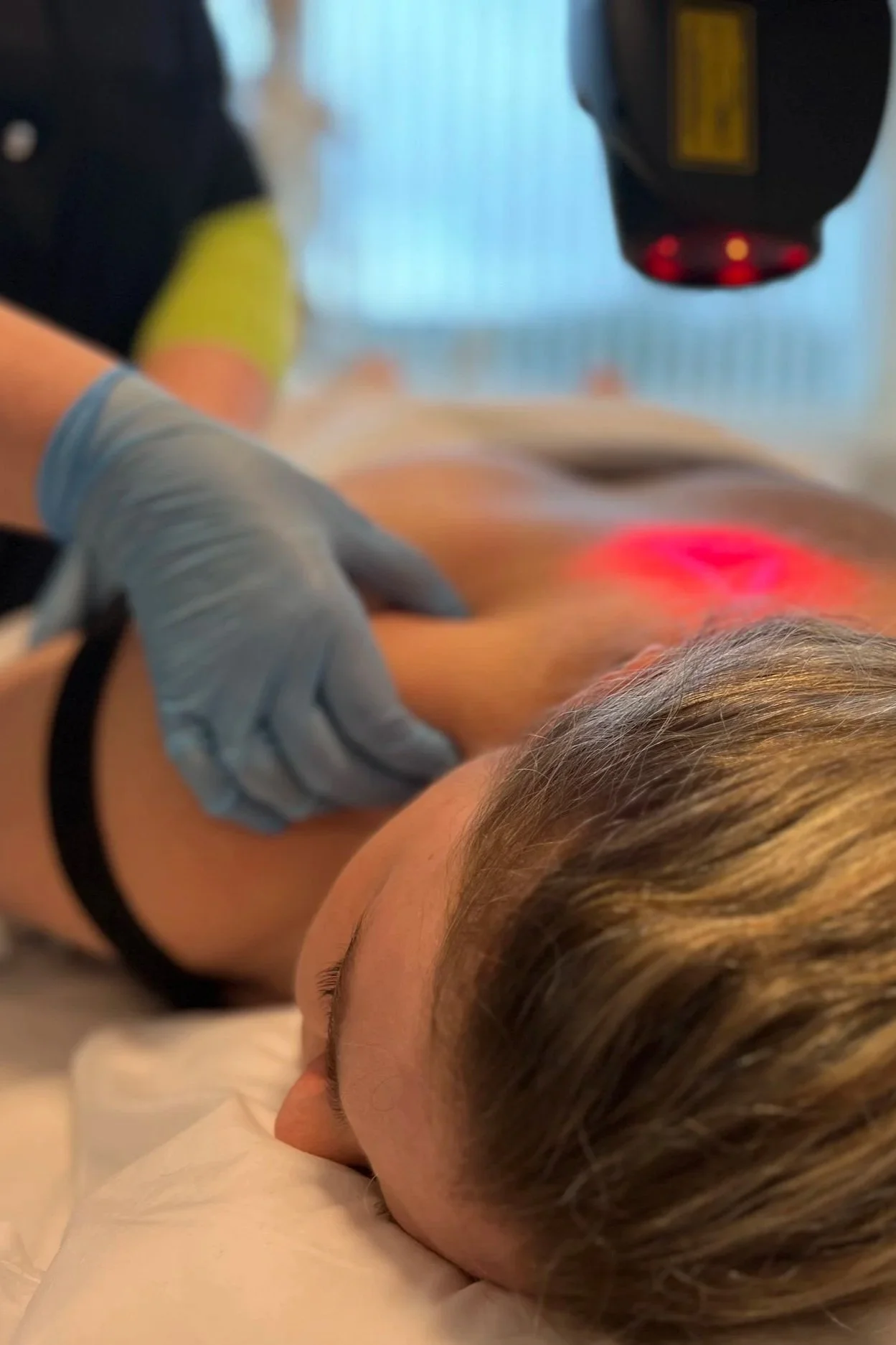 Person får laserbehandling på ryggen i en klinik, liggende på en seng med en behandler, der bruger en laser til behandling.