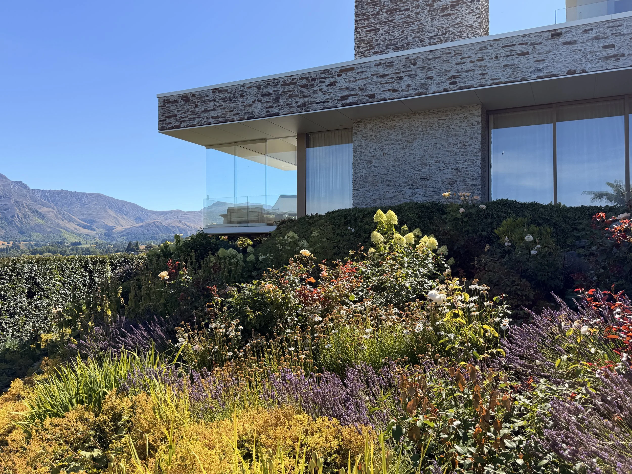 Luxury house overlooking Lake Hayes with mountains in the distance and flower garden in the foreground
