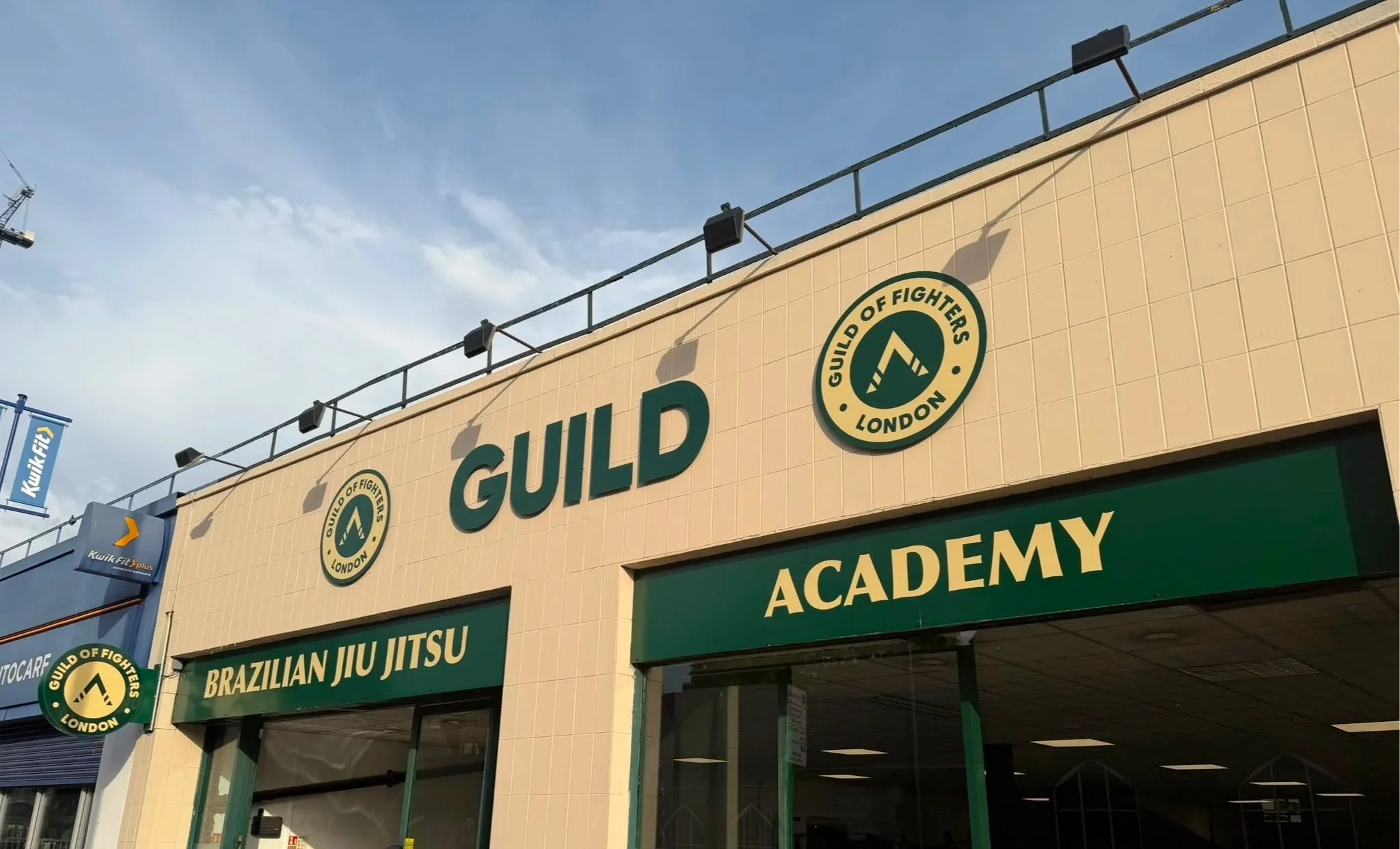 Exterior view of a building with signs for Brazilian Jiu Jitsu, Muay Thai, and MMA training, featuring the Guild of Fighters London logo.