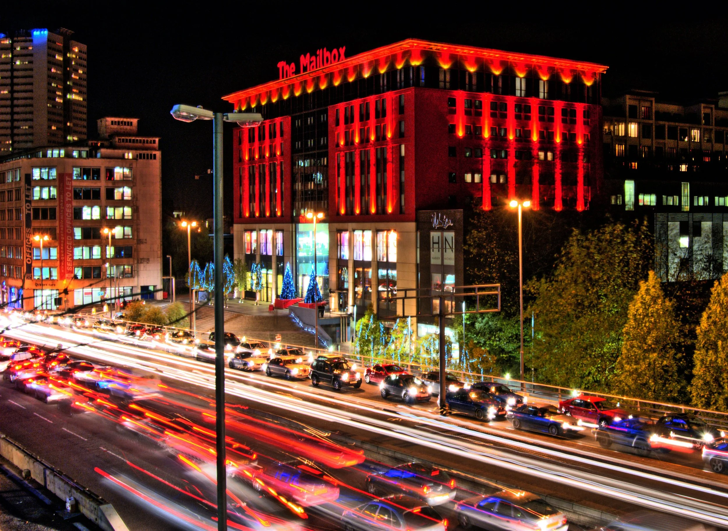Nighttime city scene with a red-lit building labeled "The Mailbox" and busy traffic on the roads.