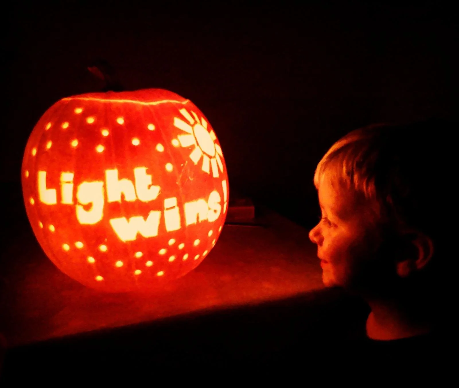 Houses of Light - A boy looking at a pumpkin carved with the words "Light wins".
