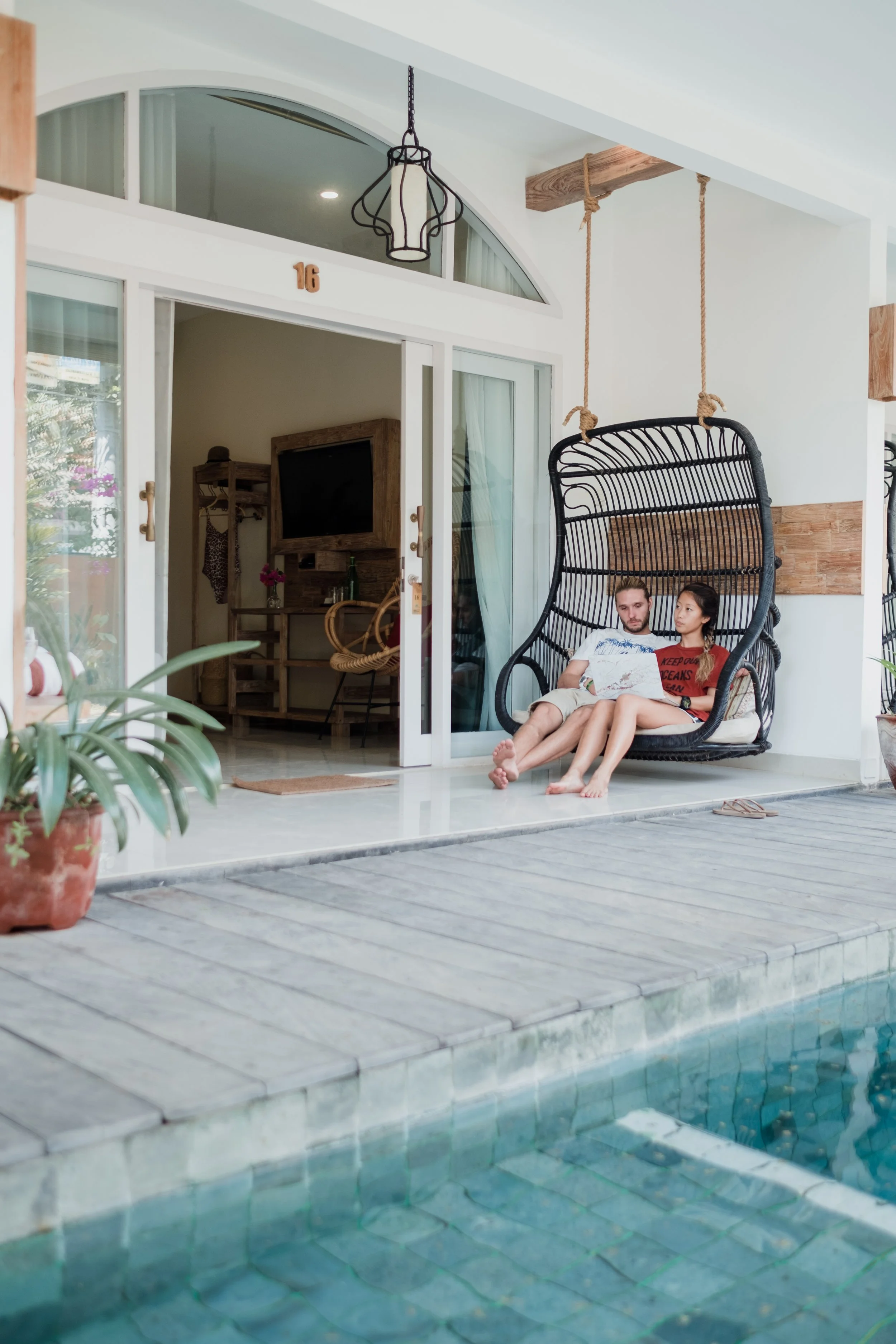 Two guests relaxing on a hanging chair beside the resort swimming pool