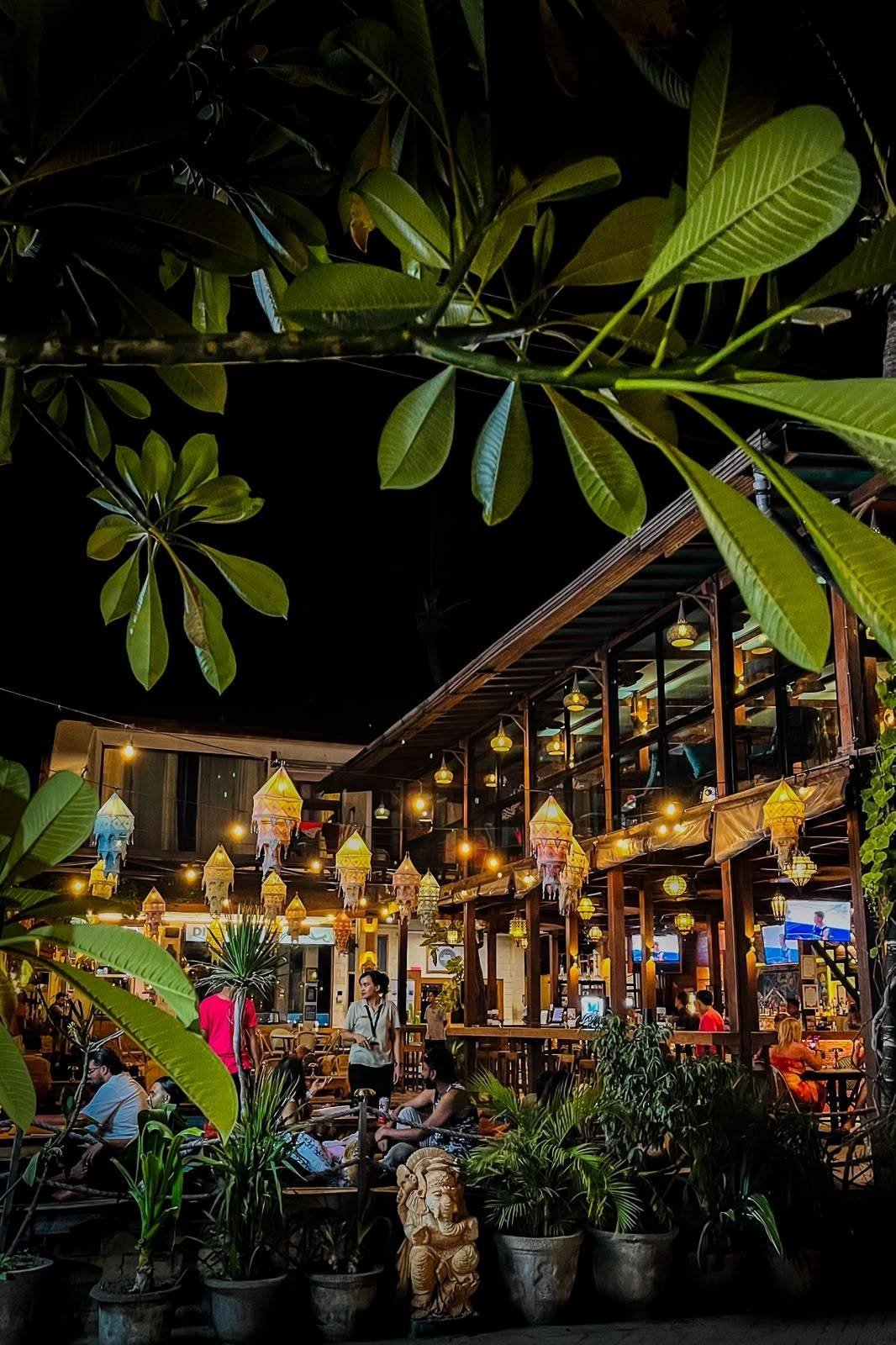Restaurants and bars illuminated at night beneath tropical trees in Gili Trawangan