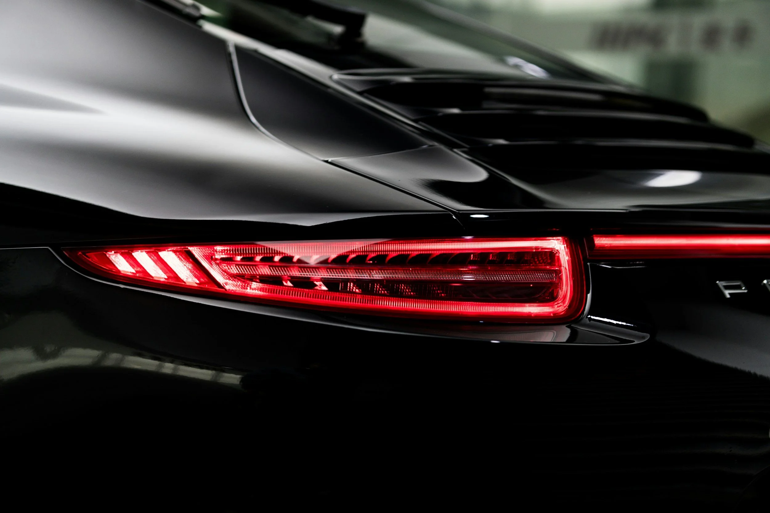 Close-up of a sleek black car showing the rear taillight and part of the back end, with a modern design and glossy finish.