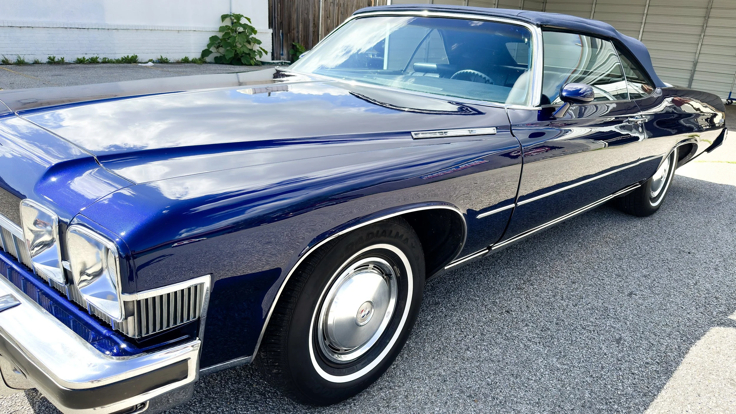 A vintage blue Cadillac convertible parked on a driveway with a garage in the background.