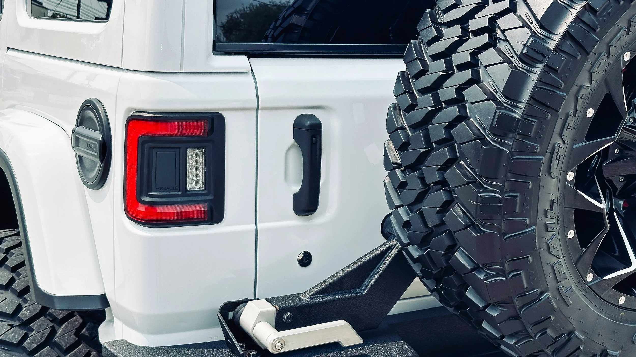 Rear view of a white off-road vehicle with large, rugged tires and a spare tire mounted on the back, close-up shot.