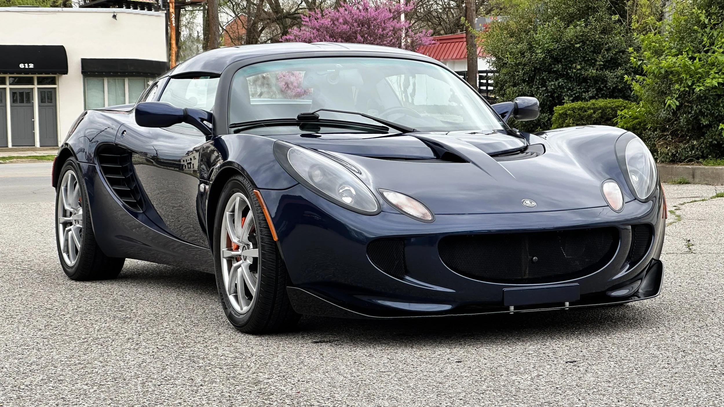 A blue convertible sports car parked on a street with trees and buildings in the background.