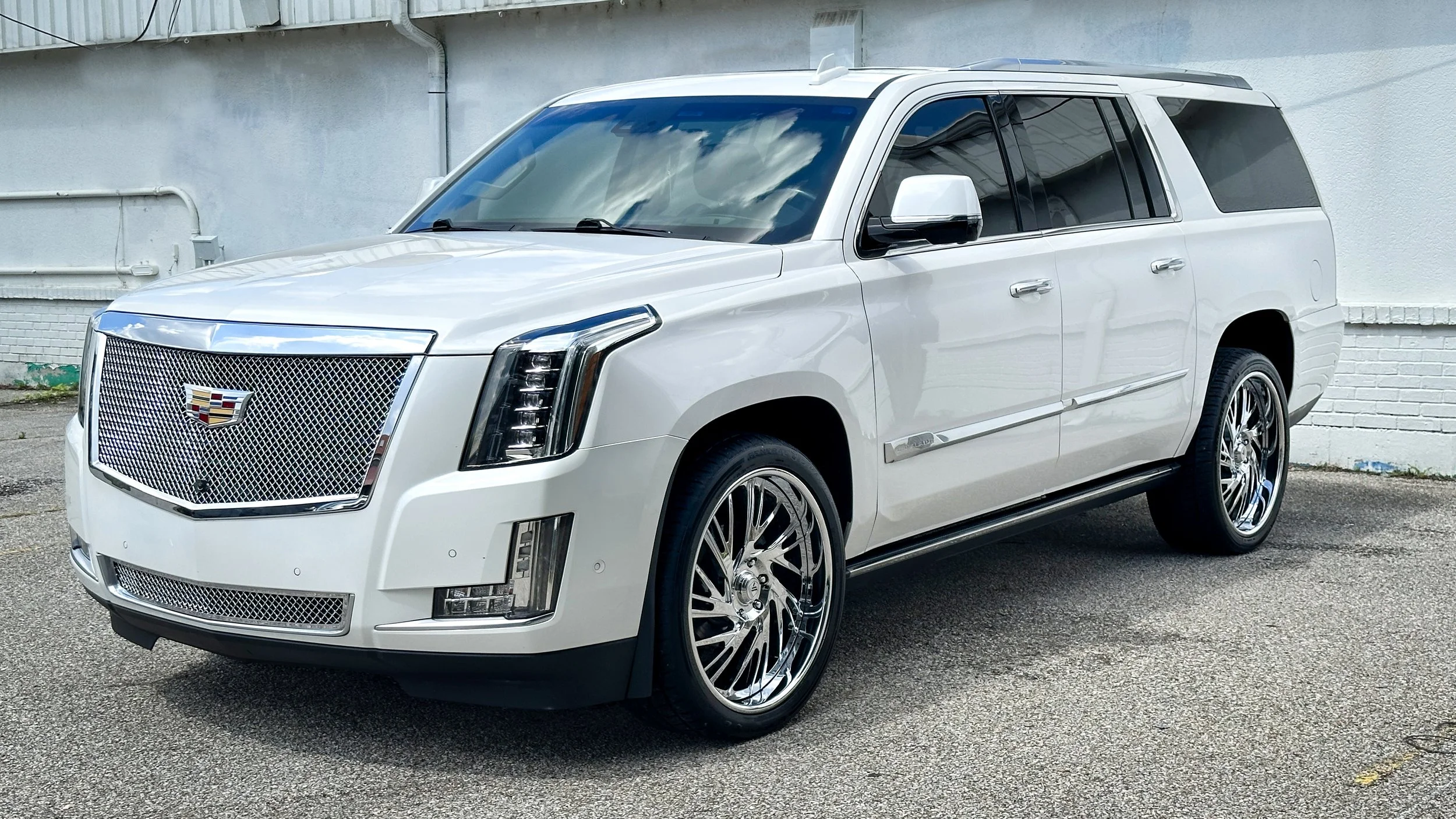 A white Cadillac Escalade parked outdoors on an asphalt surface with a plain white and gray building background.