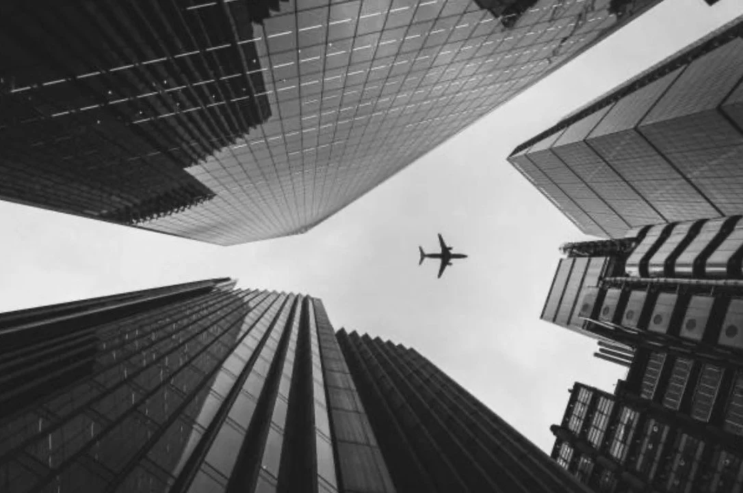 View looking up at skyscrapers with an airplane flying overhead in a city.