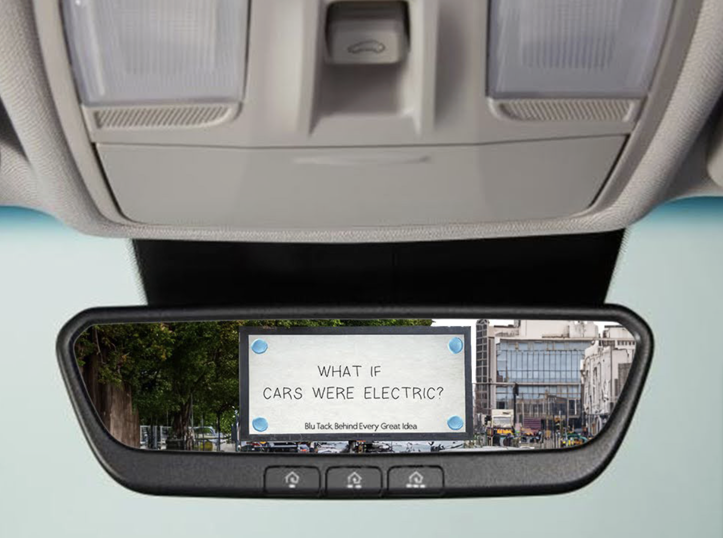 Rearview mirror with a note saying, 'What if cars were electric? Blu Tack behind every great idea,' shown in front of a cityscape with buildings and trees.
