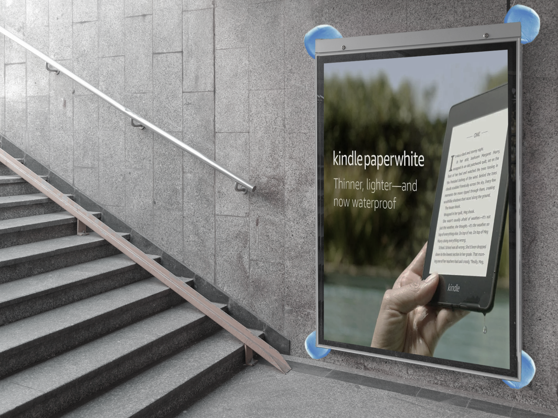 Hand holding a Kindle Paperwhite e-reader, with stairs and a large outdoor sign in the background.