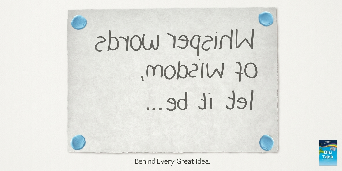A note on a wall reads flipped text: "Wisper words of wisdom, let it be..." with four blue push pins at the corners. Below the note, it says "Behind Every Great Idea." in small black text, and in the bottom right corner, there's a small blue pack of BluTack.