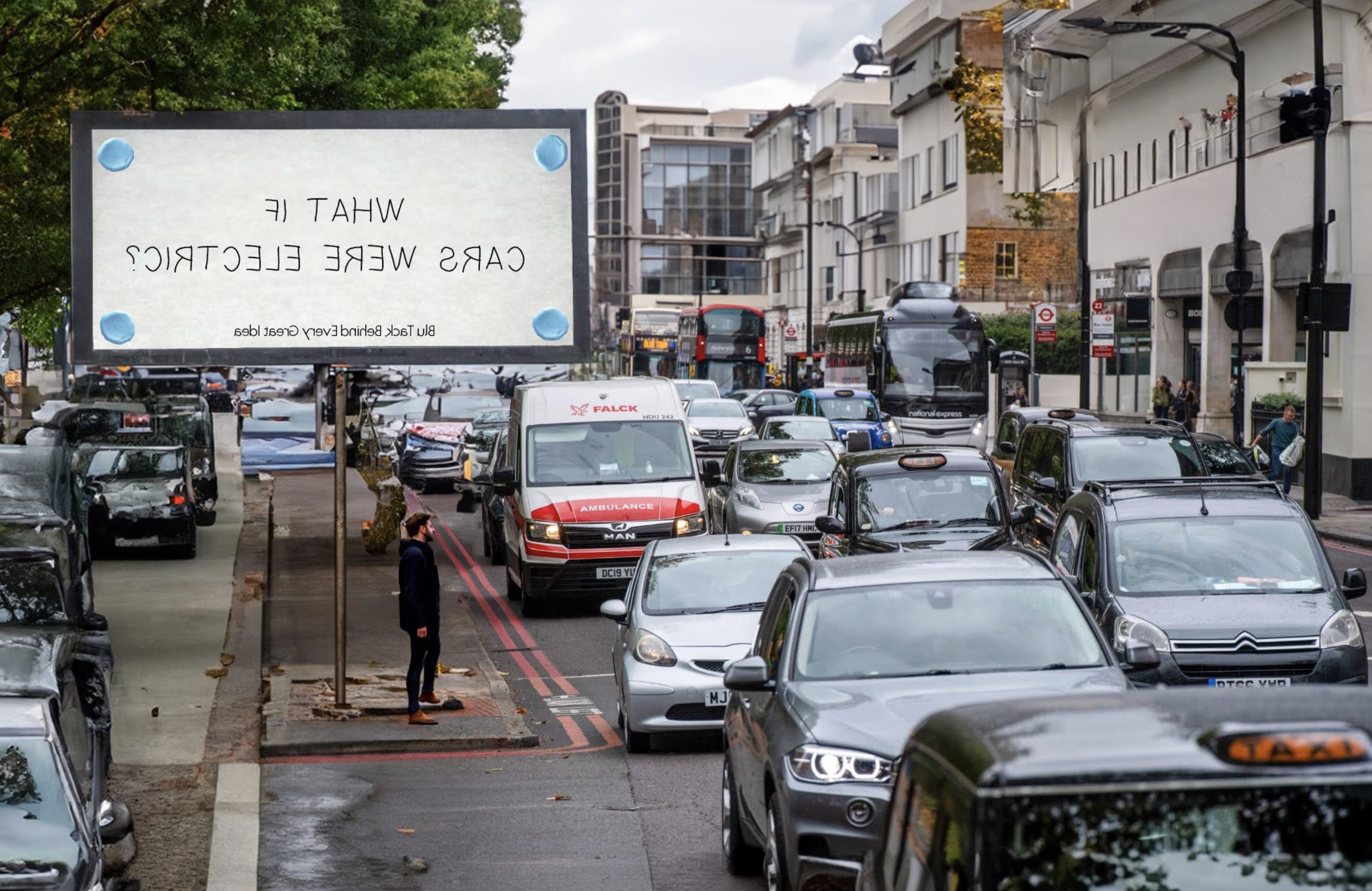 Street scene with a large billboard that reads, "WHAT IF CARS WERE ELECTRIC?" and shows a parking lot filled with various cars, trucks, and buses, with buildings and trees in the background.
