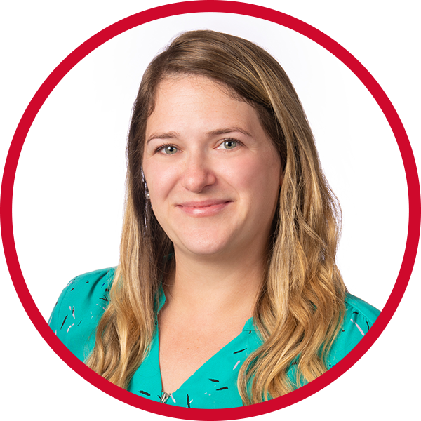 Portrait of a woman with long blonde hair wearing a teal top, smiling, against a white background with a red circular border.
