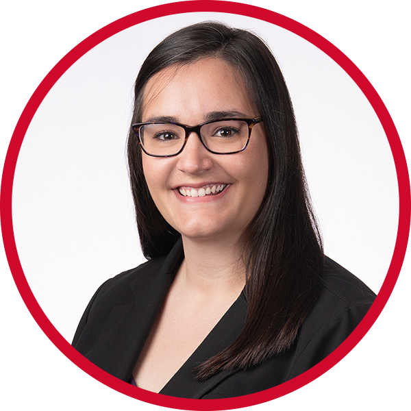 A woman with straight dark hair wearing glasses and a black blazer, smiling against a white background with red circular design.