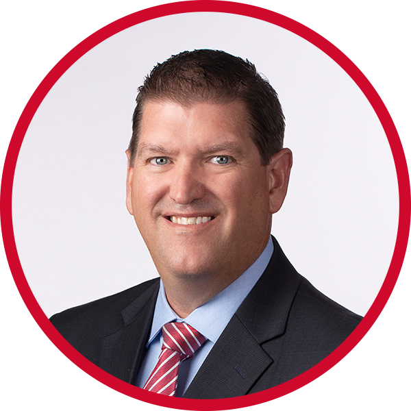 Professional headshot of a smiling man in a business suit against a white background with a red circular border.
