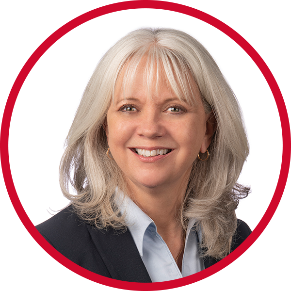 A professional woman with shoulder-length gray hair, wearing a dark blazer and light blue shirt, smiling against a white background with a red border.
