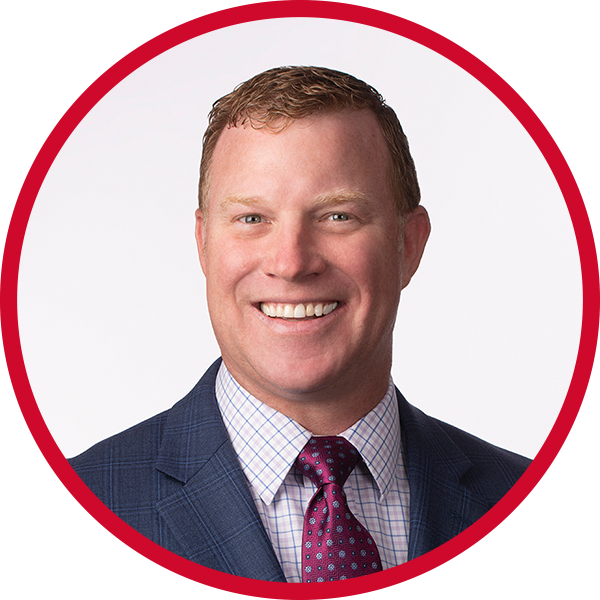 Portrait of a man with short red hair, wearing a dark blue plaid suit, checkered shirt, and patterned tie, smiling.