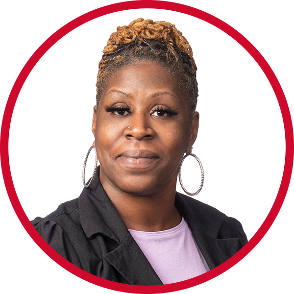 Portrait of an African American woman with short, curly blonde hair, wearing hoop earrings, a black blazer, and a light purple shirt against a red background.