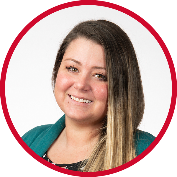 Portrait of a young woman with long brown hair, smiling, wearing a green blazer, with a red and white background.
