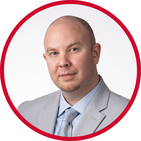 Headshot of a man in a light gray suit with a light blue shirt and striped tie, against a white background with a red circular border.