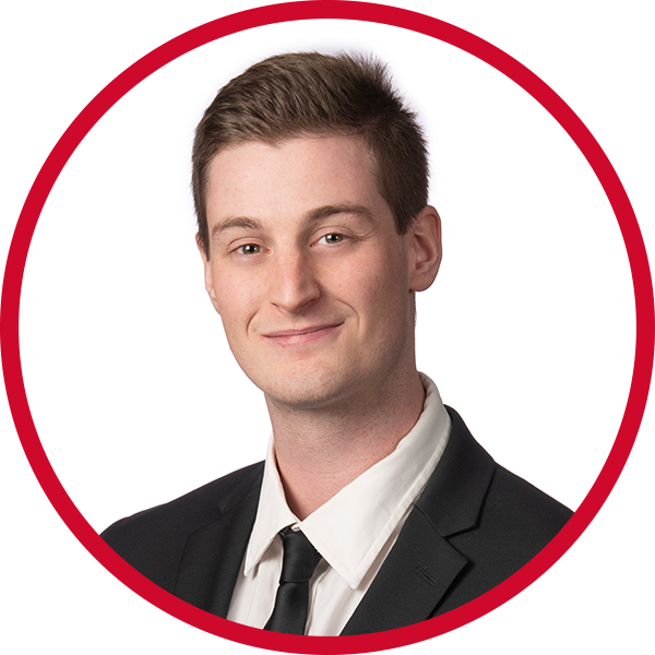 Portrait of a young man in a business suit smiling against a red and white background.