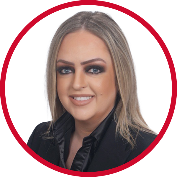 A woman with blonde hair, blue eyes, and makeup, wearing a black blazer and smiling, against a white background with a red circular border.
