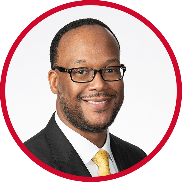 portrait of a smiling African American man wearing glasses, a black suit, white shirt, and yellow tie, against a white background with a red border.