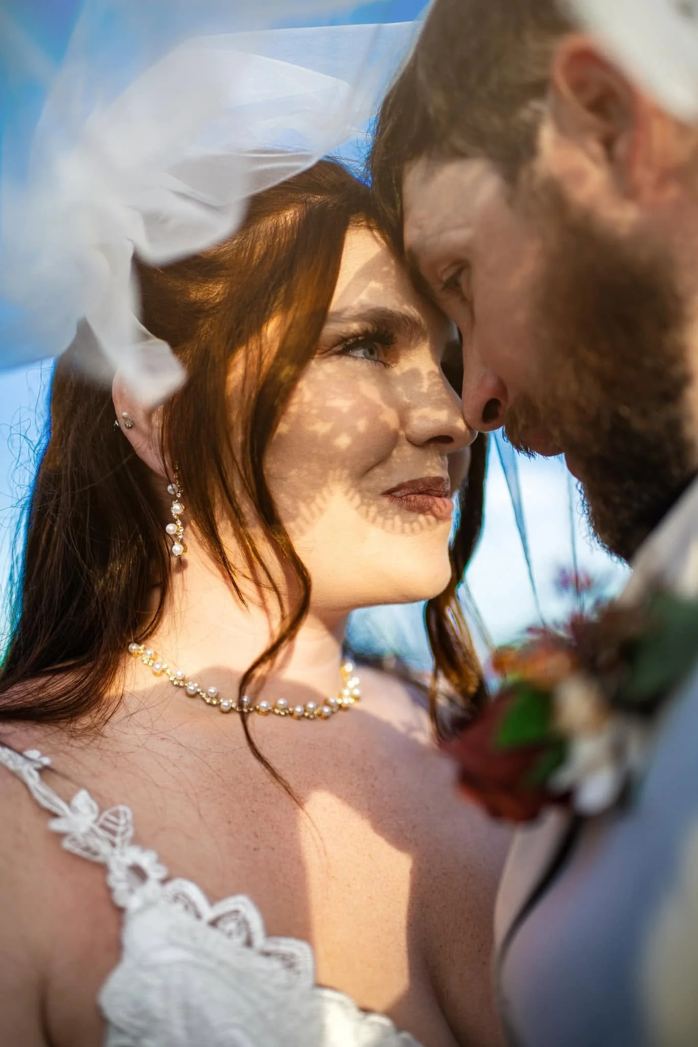 A close-up of a bride and groom face-to-face, touching foreheads during their wedding ceremony, with a blue and light background.