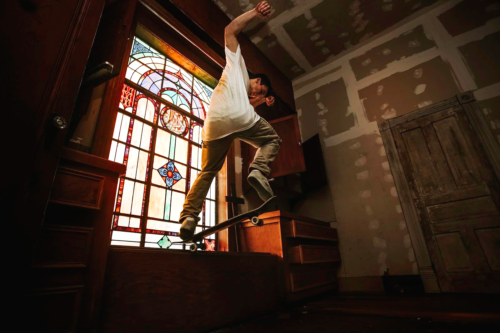 Person skateboarding inside a room with a large stained glass window and unfinished walls.
