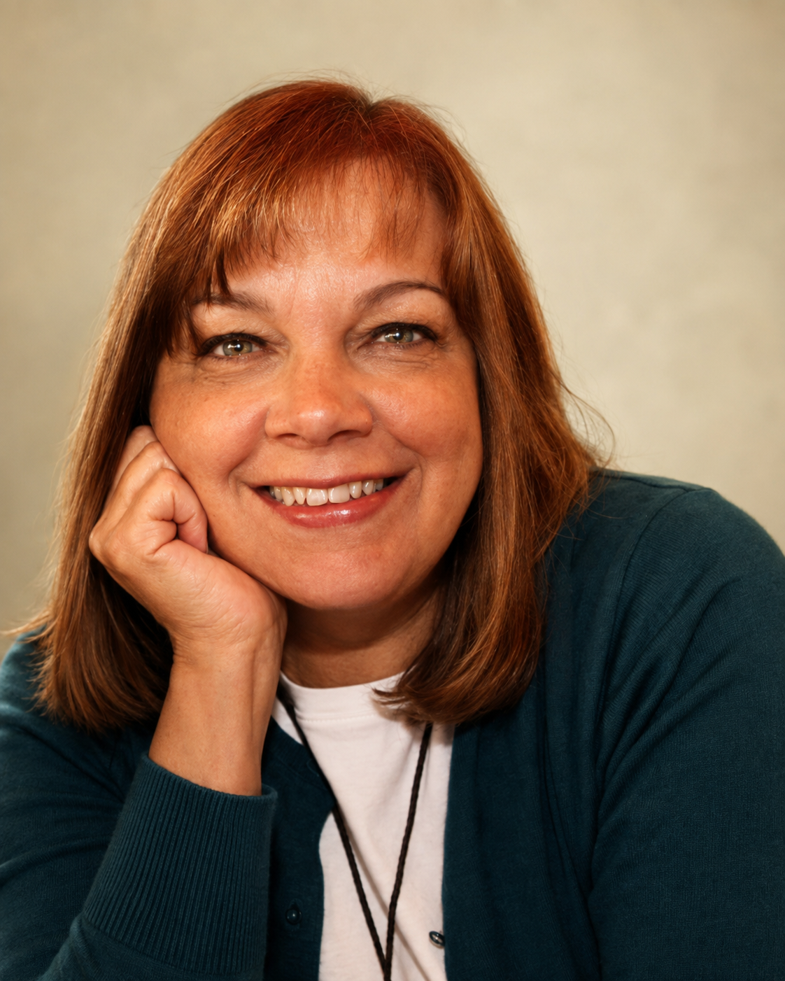Close-up portrait of Janet Morris Belvin, resting her face on her hand, wearing a dark blue sweater and a white t-shirt, against a neutral background.