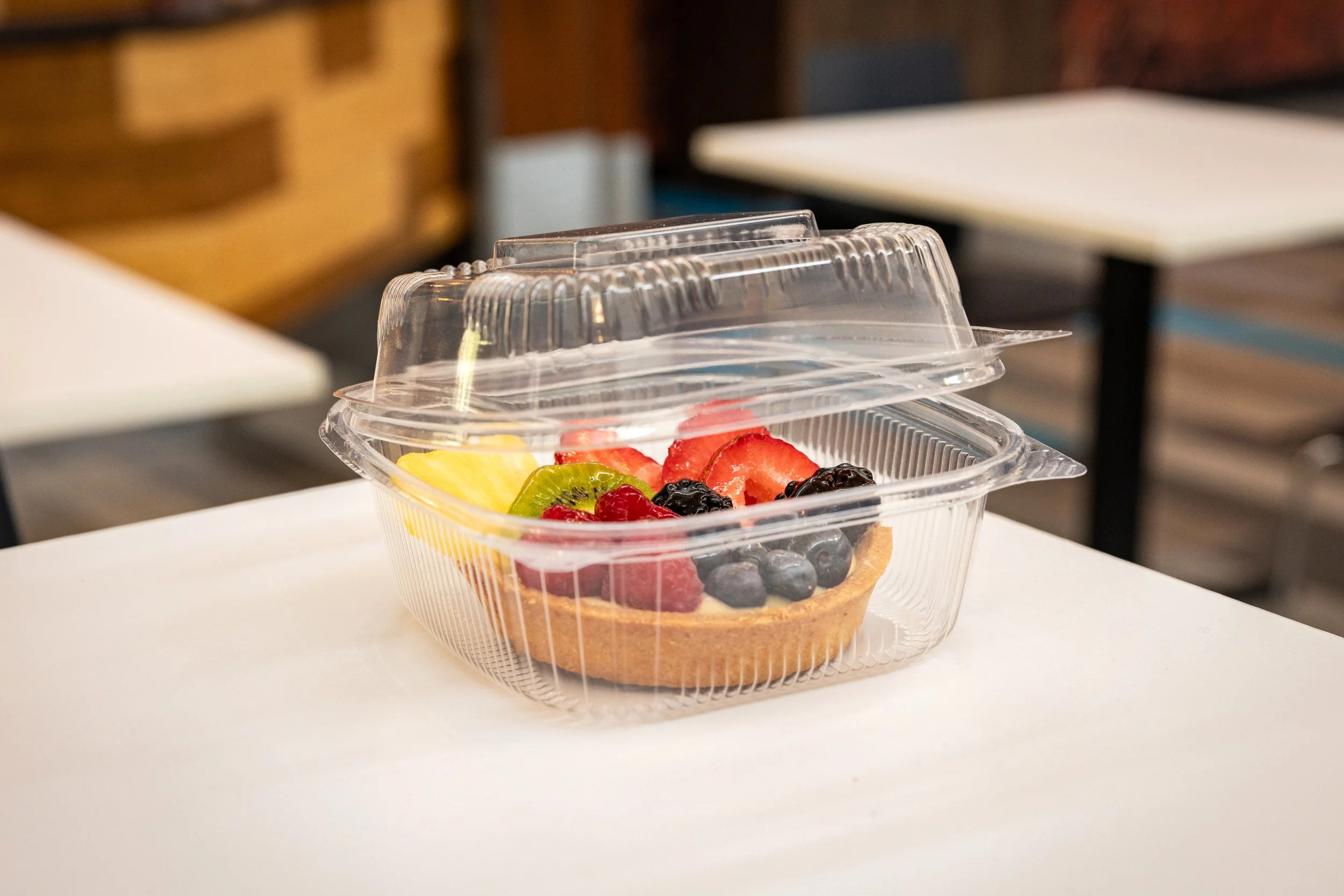 Close-up of a plastic container with a layered fruit tart topped with fresh strawberries, blueberries, blackberries, kiwi, and raspberries, with a partly visible waffle crust underneath.