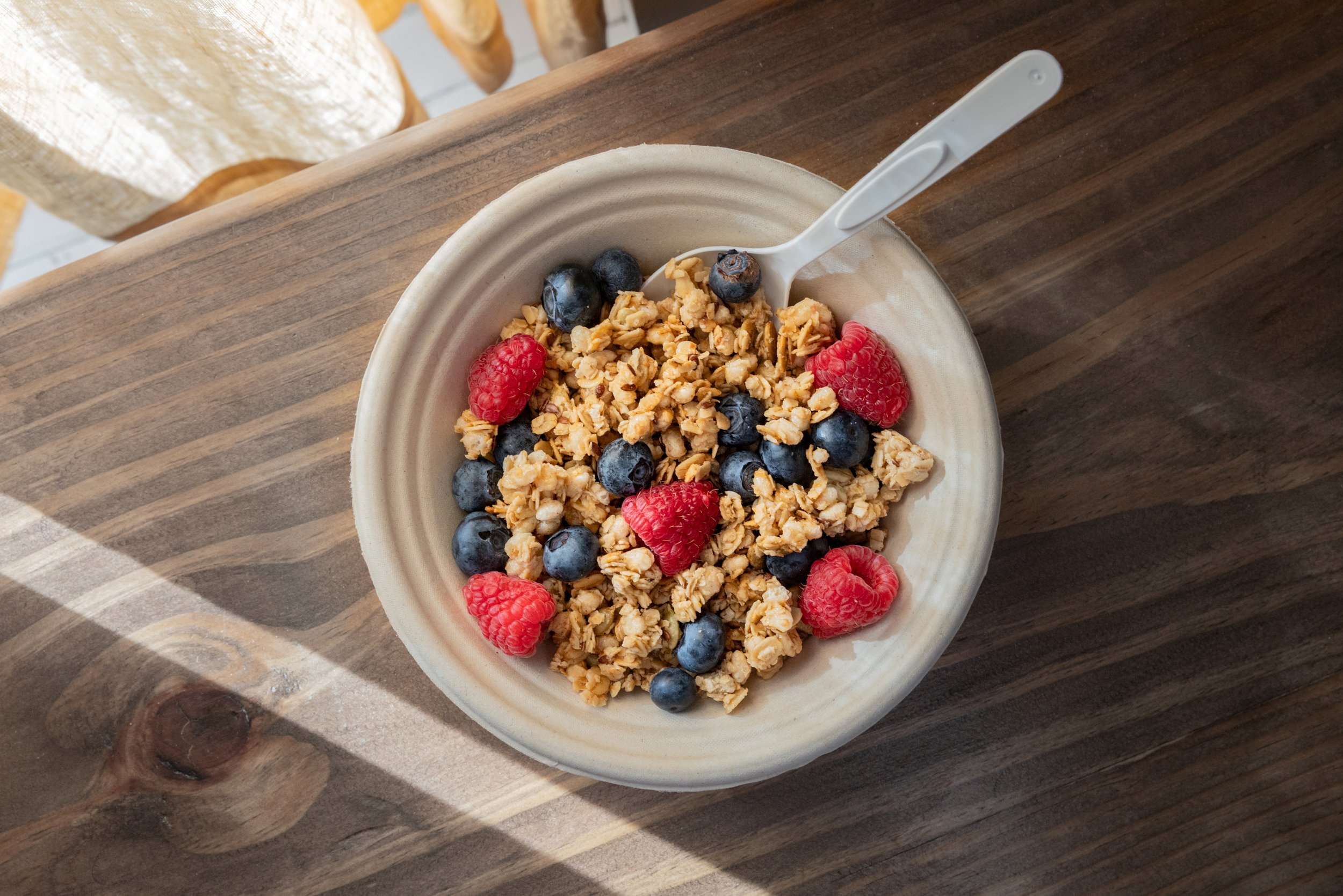 A bowl of granola topped with blueberries and raspberries on a wooden table.