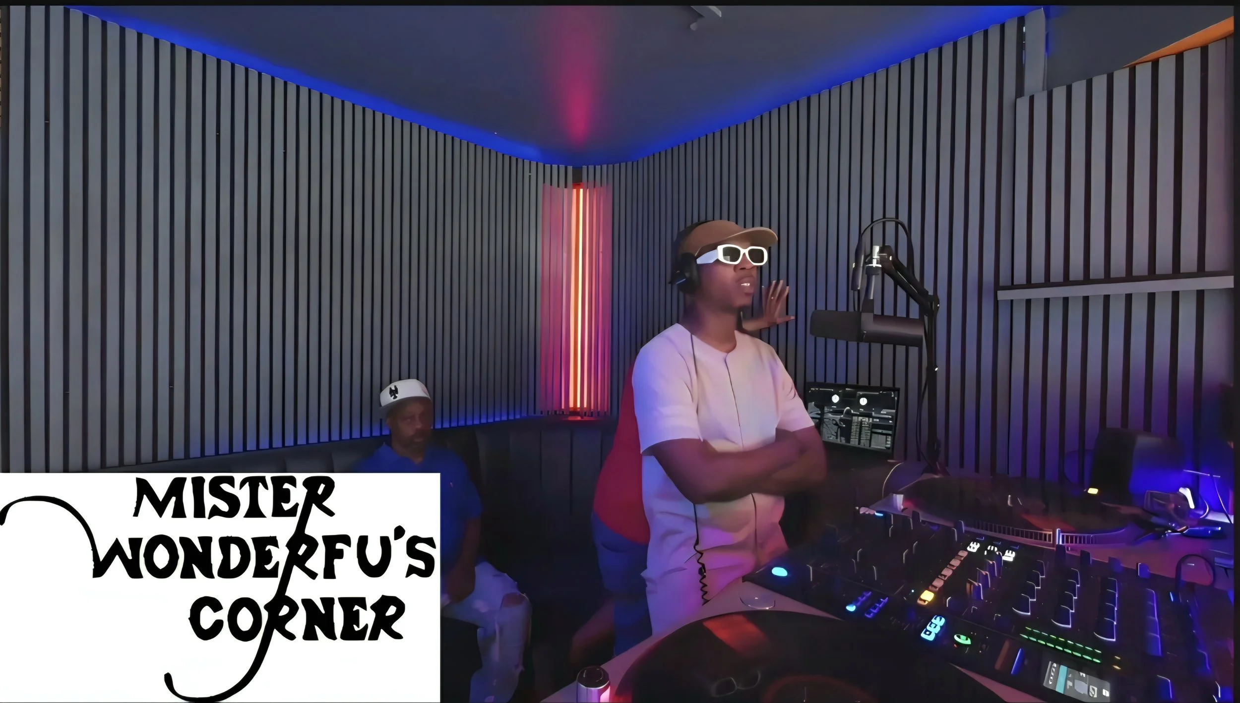 A person wearing white sunglasses and headphones stands in a recording studio with colorful neon lighting, DJ equipment, and a sign that reads 'MISTER WONDERFUL'S CORNER'.