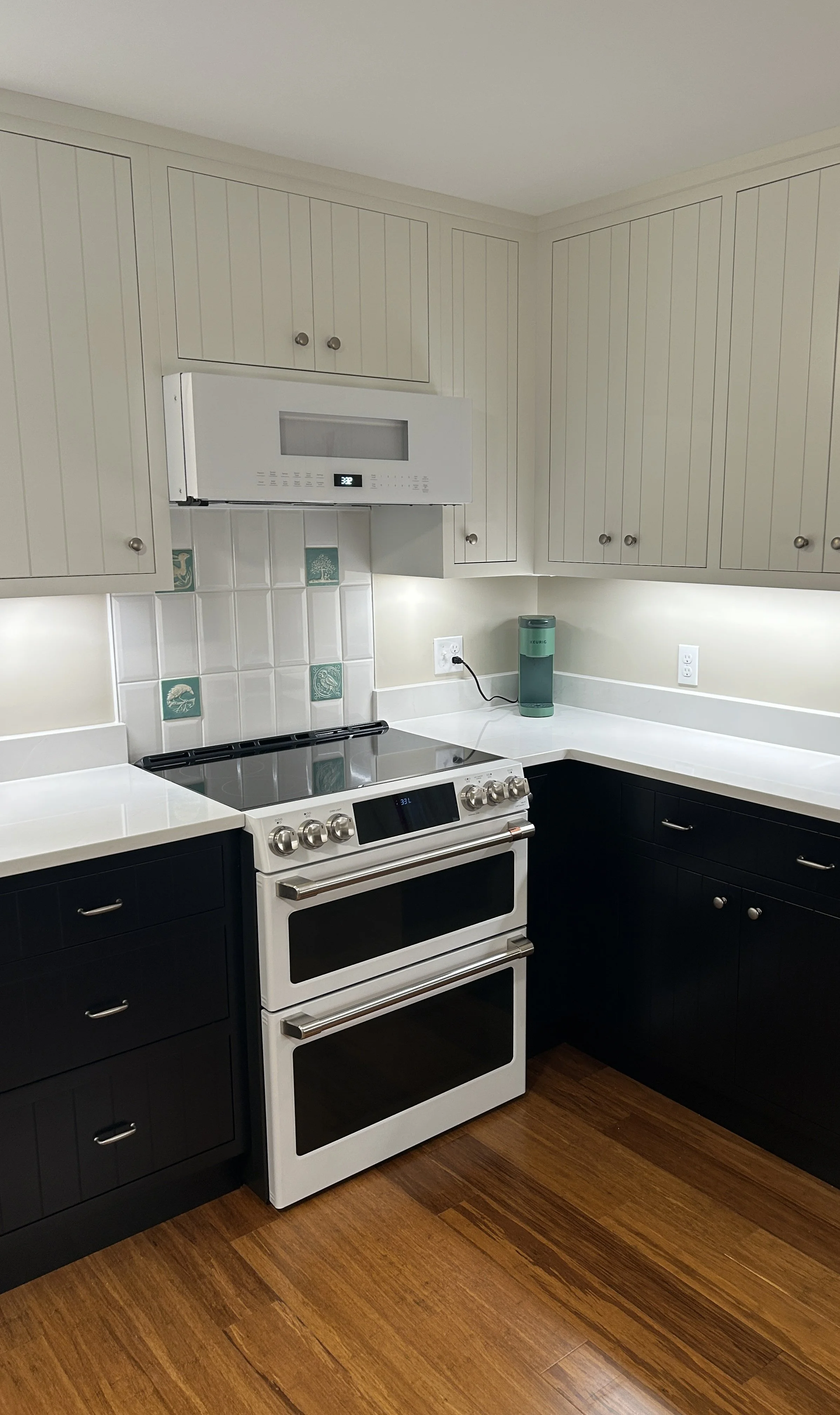 Kitchen with white upper cabinets, black lower cabinets, a white stove, a microwave, and a countertop with a teal water filter.