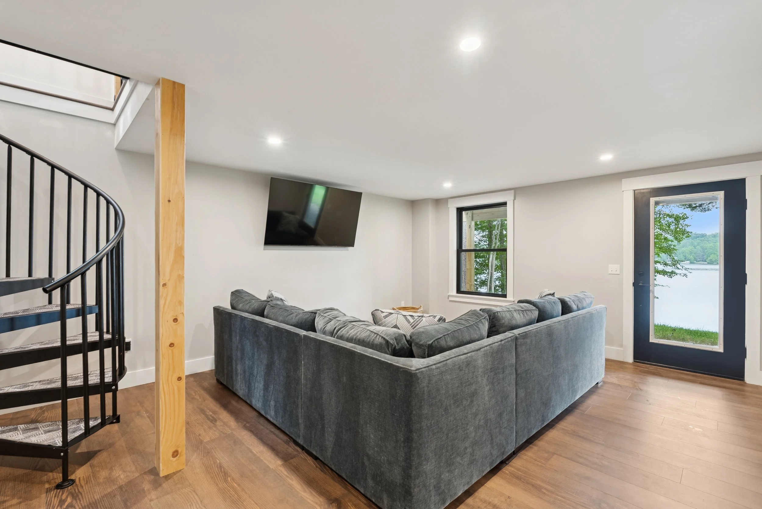 Living room with gray sofa, large window, and flat-screen TV on the wall.