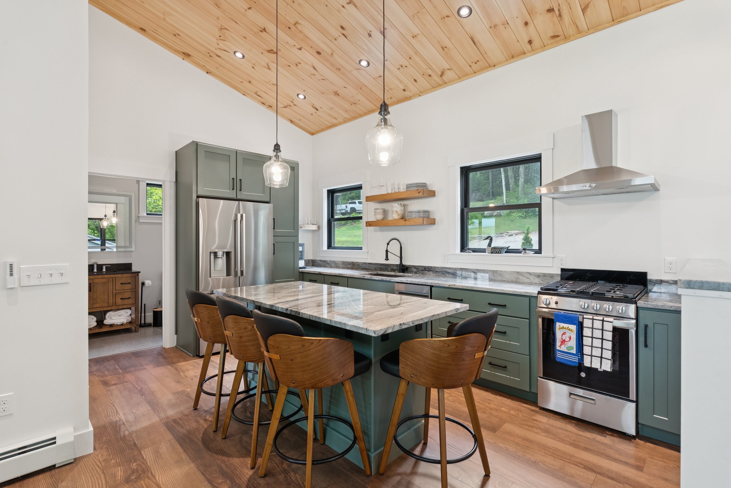 Modern kitchen with a wooden ceiling, pendant lights, gray cabinets, a stainless steel refrigerator, and a kitchen island with wooden chairs.