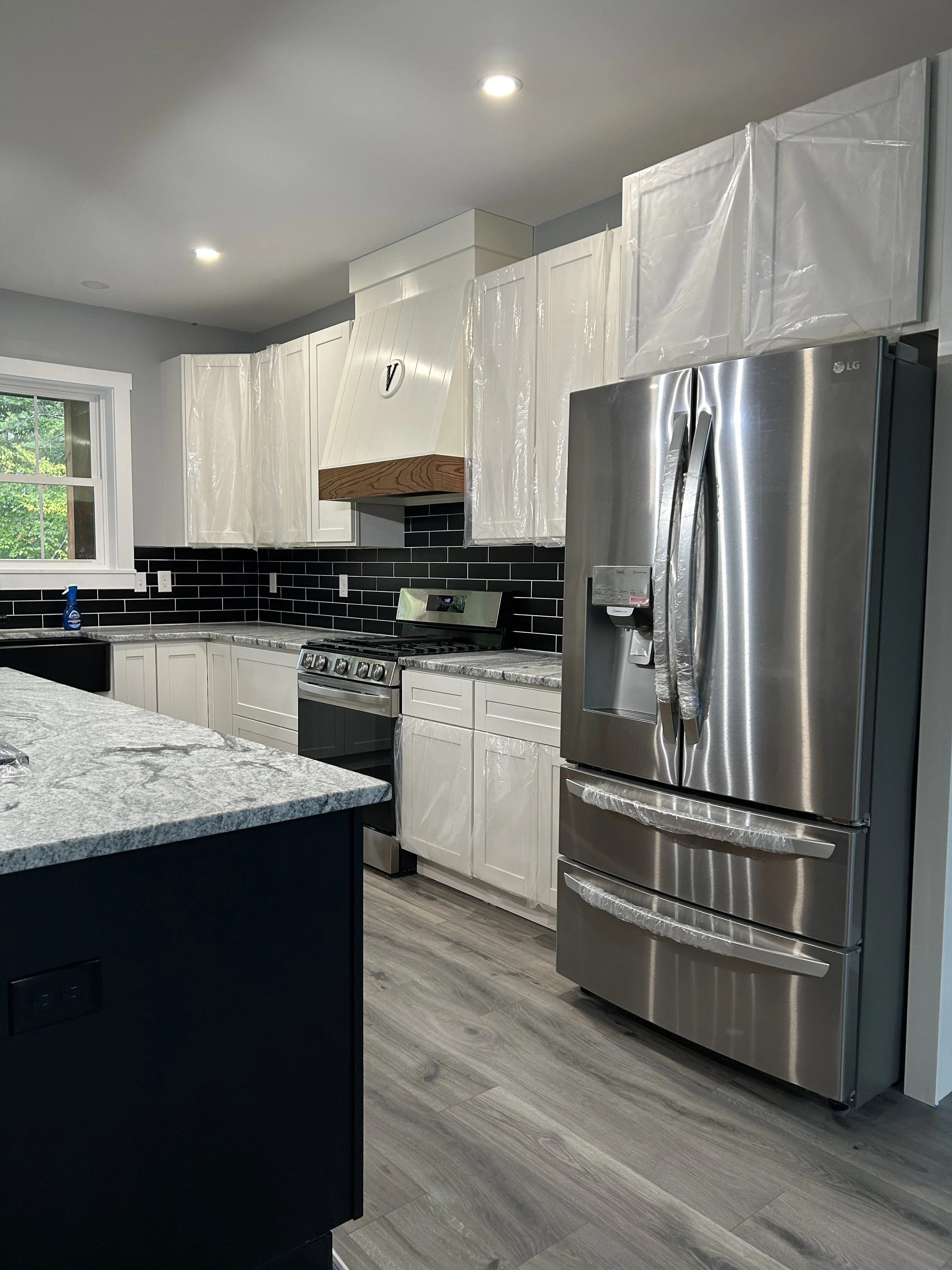 Modern kitchen with white cabinets, black backsplash, stainless steel refrigerator, stove, and a window with greenery outside.