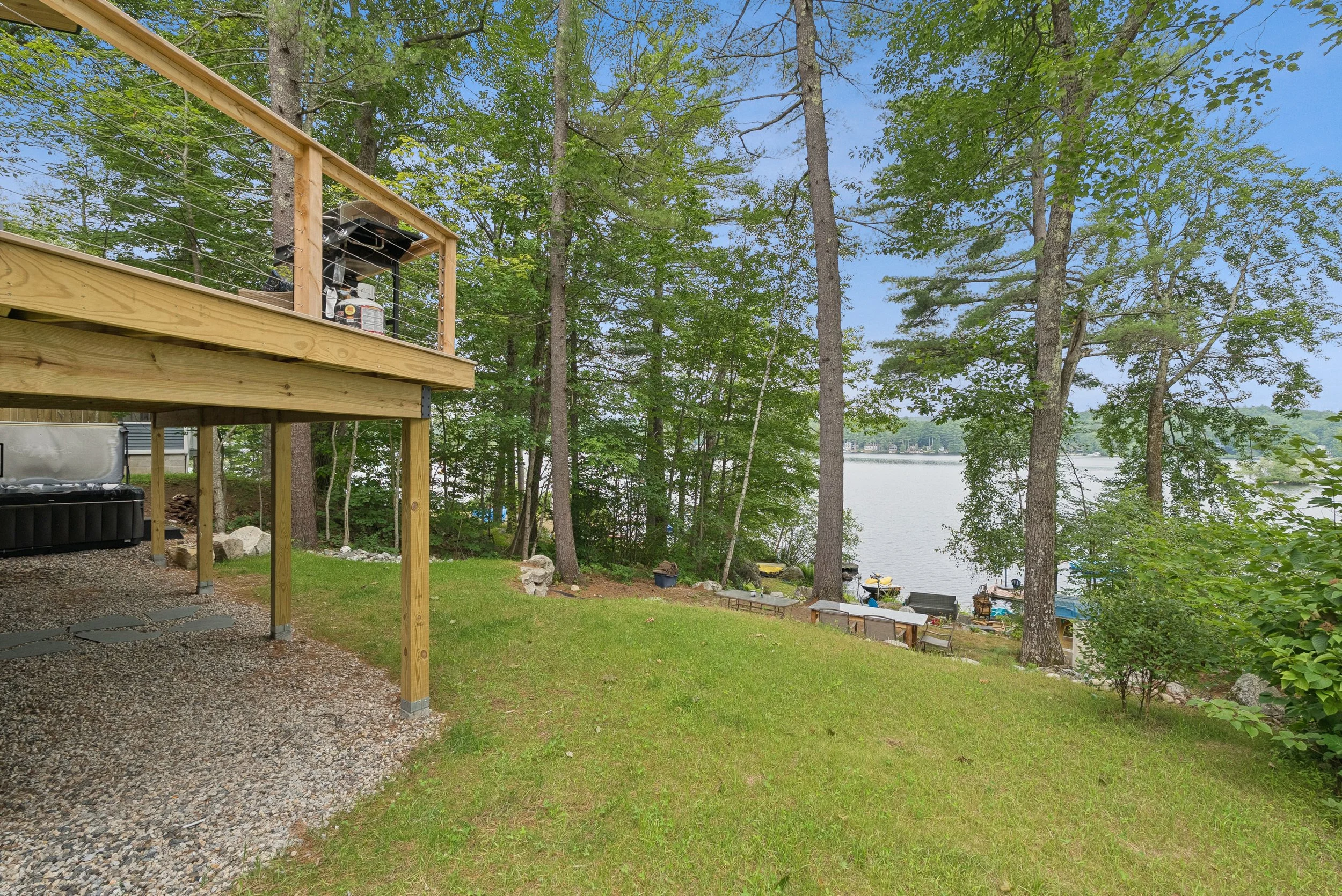 A wooden deck overlooking a water body with trees surrounding it, with a grill on the deck and boats visible on the lake.