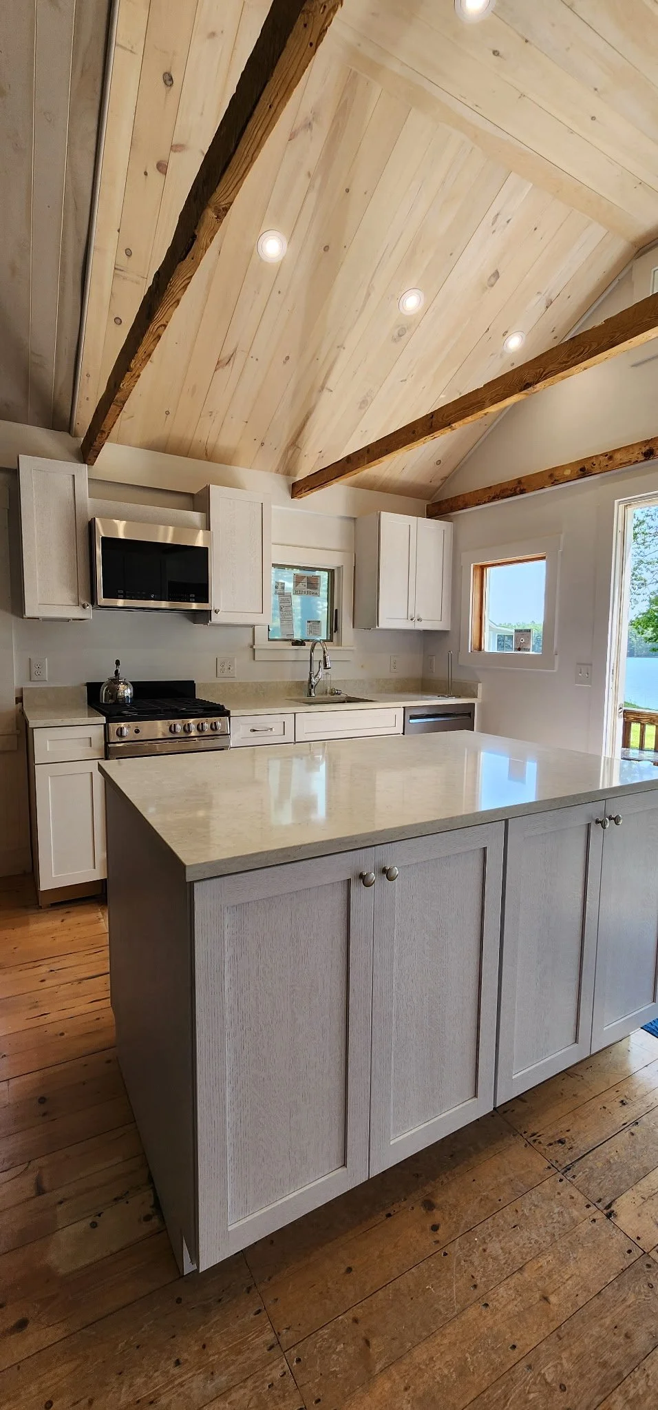 Kitchen with a wooden ceiling, white cabinets, marble island, stainless steel appliances, and hardwood flooring.