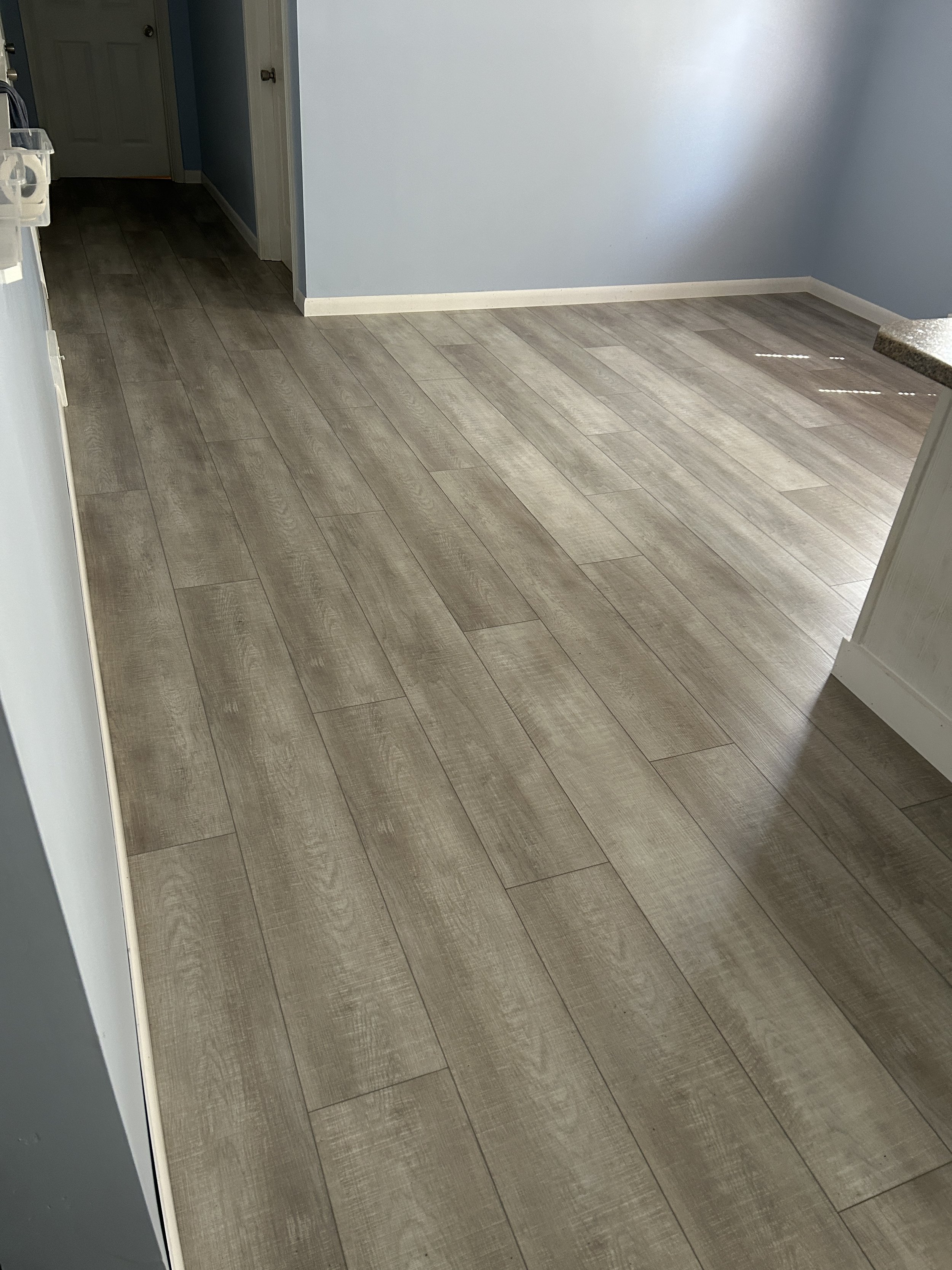 Empty room with grey vinyl flooring, gray outlined walls painted in light blue, and a small step at the edge near a granite countertop.